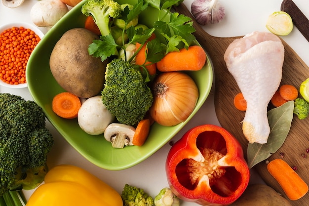 Free photo top view mix of vegetables on cutting board and in bowl with chicken drumstick