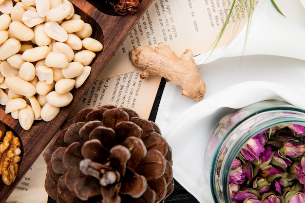 Top view of mixed nuts and dried fruits, dry rose buds in a glass jar and pine cone on white