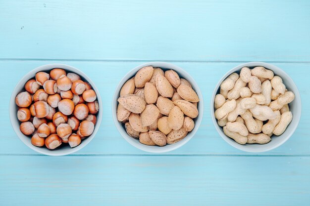 Top view of mixed nuts hazelnuts almond and peanuts in shell in bowls on blue wooden background