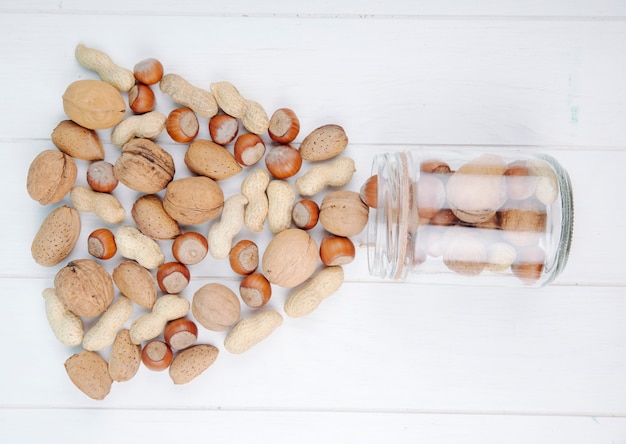 Top view of mixed nuts scattered from a glass jar on white background