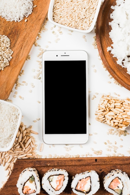 Top view of mobile phone surrounded with sushi and variety of uncooked rice