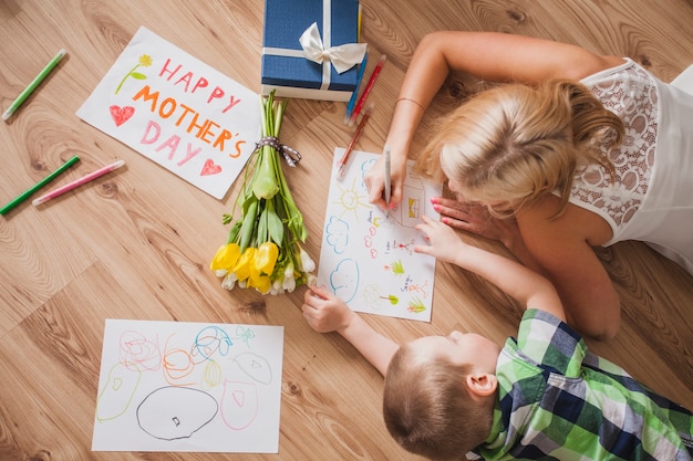 Top view of mother and son drawing next to a mother's day poster