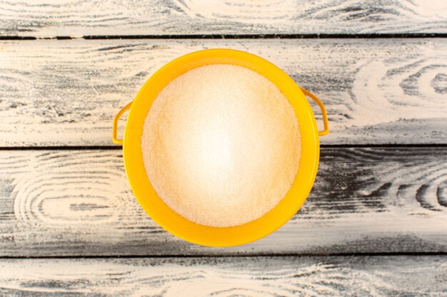 A top view much salt inside yellow round plate on the grey rustic wooden desk