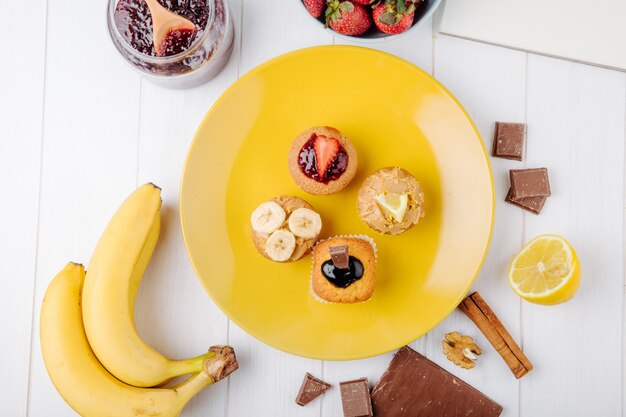 Top view muffins with bananas strawberries chocolate and lemon on a yellow plate