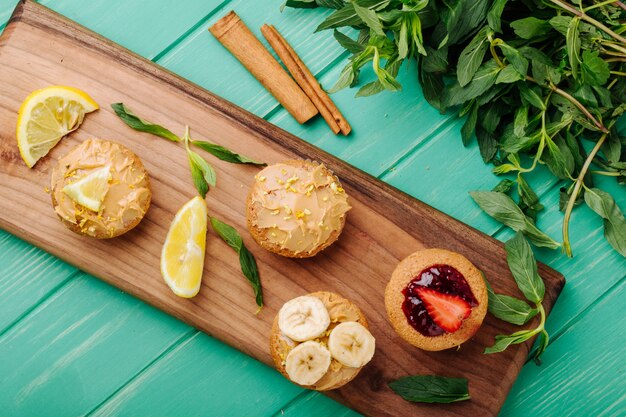 Top view muffins with strawberries banana and lemon on a board with cinnamon and mint