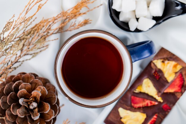 Top view of a mug of tea and pine cone with chocolate bar on white