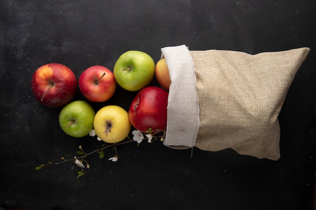 Top view multi-colored apples in a burlap bag with a branch of flowers