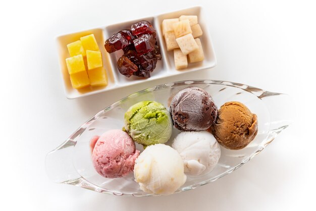 Вид сверху разноцветного мороженого в прозрачном блюде и сладких обработанных фруктов для совместной трапезы в винтажном тайском стиле, набор красочных шариков мороженого разных цветов на белом фоне стола