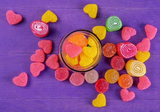 Top view multi-colored marmalade in a jar on a purple background