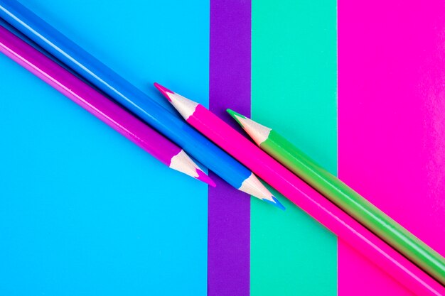 Top view multi-colored pencils on a pink light green purple and blue background