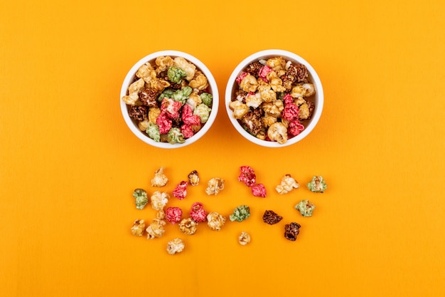 Top view of multi-colored popcorn in bowls on yellow horizontal