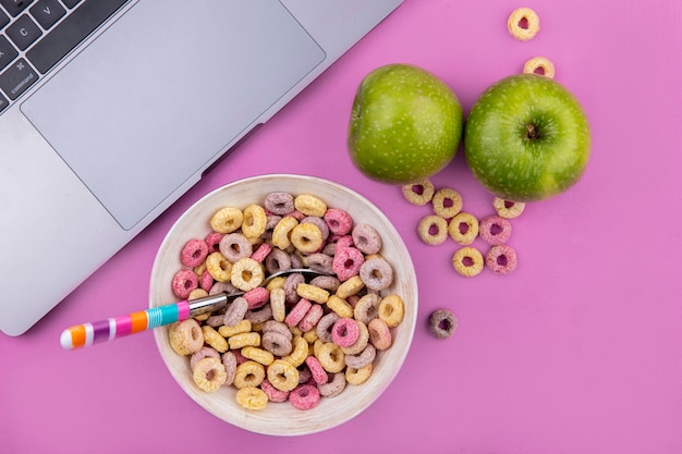 Free photo top view of multicolored cereals on a bowl with colorful spoon with green apples on pink surface