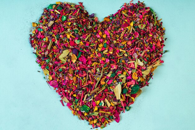 Top view of multicolored dried flower petals blooms and herbs arranged in a heart shape on blue