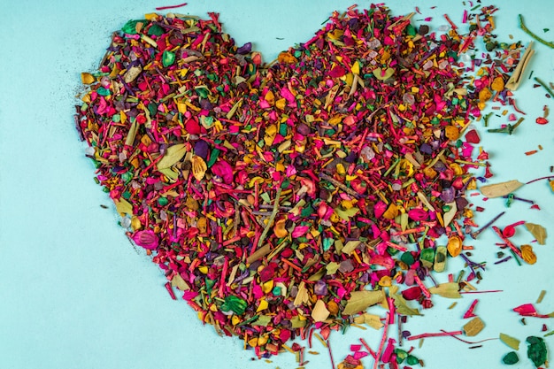 Top view of multicolored dried flower petals blooms and herbs arranged in a heart shape on blue