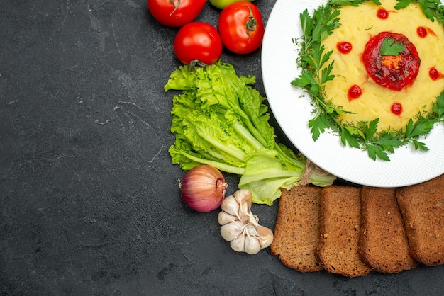 Top view of mushed potato dish with dark bread loafs and vegetables on dark