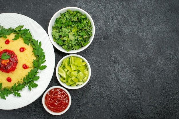 Top view of mushed potato dish with tomato sauce and greens on dark grey