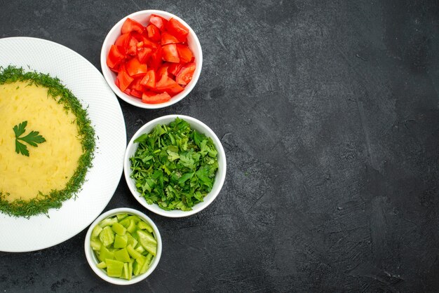 Top view of mushed potatoes with greens and fresh sliced tomatoes on dark grey