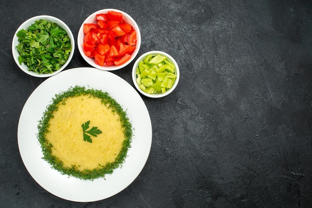 Top view of mushed potatoes with greens and sliced tomatoes on grey