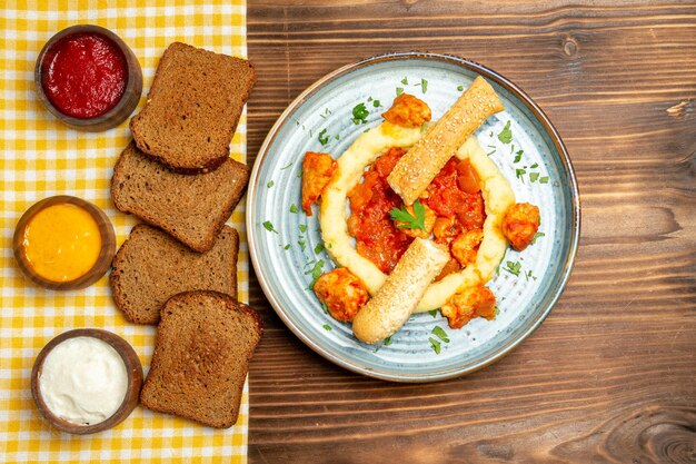 Вид сверху на картофельное пюре с соусом из кусочков курицы и хлеба на коричневом столе, блюдо из картофеля, обед, мясо