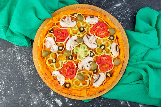 Top view mushroom pizza with red tomatoes olives mushrooms all sliced inside with oil on the grey desk green tissue pizza dough italian