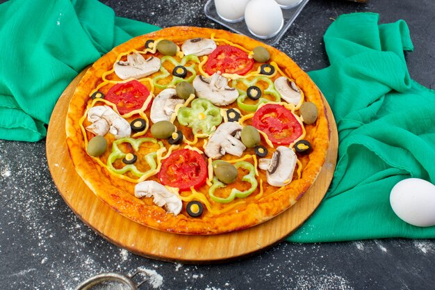 토마토 올리브 버섯이있는 상위 뷰 버섯 피자 회색 책상에 밀가루로 내부 슬라이스 녹색 조직 피자 반죽 이탈리아 음식