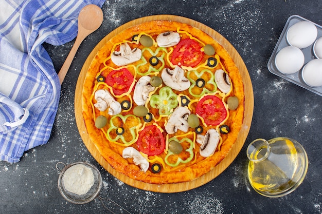 灰色の机の上に小麦粉とトマトオリーブキノコとキノコのピザのトップビューピザ生地イタリア料理