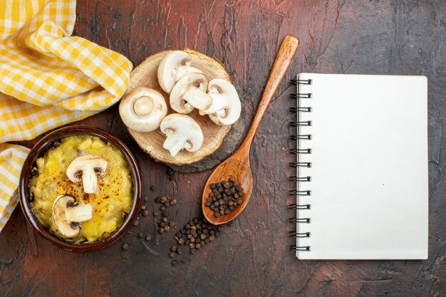 Top view mushroom with mosarella in bowls black pepper in wooden spoon mushrooms on wood board notebook on dark red table