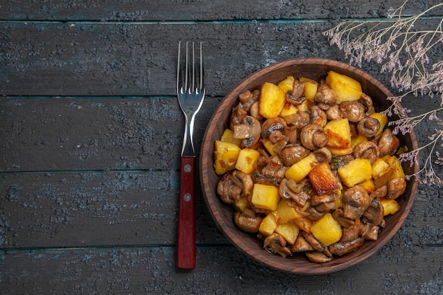 Vista dall'alto funghi e patate patate con funghi in una ciotola tra una forchetta e rami di alberi