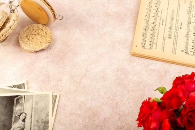 Un libro di note musicali con vista dall'alto aperto insieme a patatine di rose rosse e foto in rosa