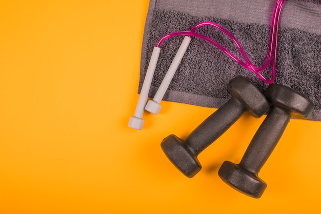 Top view of napkin with skipping rope and black dumbbells on yellow background