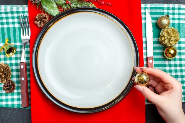 Top view of national Christmal meal background with empty plates cutlery set holding one of decoration accessories on green stripped towel