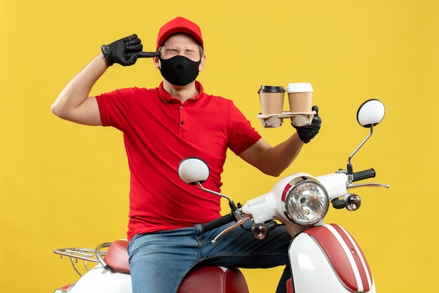 Top view of nervous delivery guy wearing uniform and hat gloves in medical mask sitting on scooter showing orders