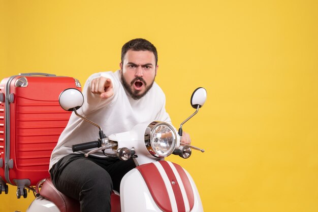 Top view of nervous young guy sitting on motorcycle with suitcase on it and pointing forward on isolated yellow background