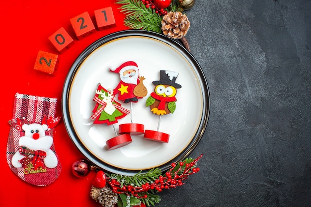 Top view of New year background with dinner plate decoration accessories fir branches and numbers christmas sock on a red napkin on a black table