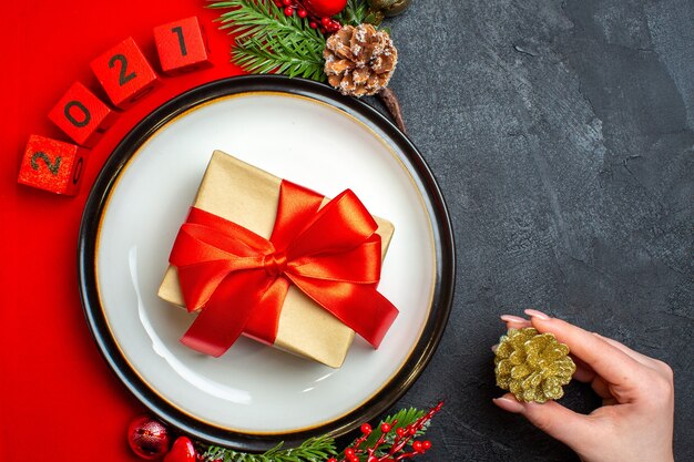 Top view of New year background with gift on dinner plate decoration accessories fir branches and numbers on a red napkin on a black table