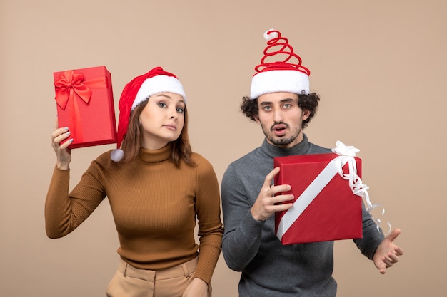 Vista dall'alto del concetto di umore e festa del nuovo anno - coppia adorabile confusa che tiene i regali che indossano cappelli di babbo natale su grigio