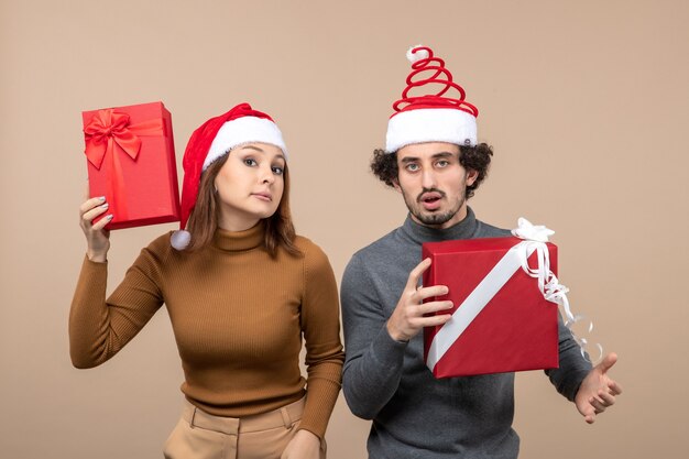 Top view of new year mood and party concept - confused lovely couple holding gifts wearing santa claus hats on gray