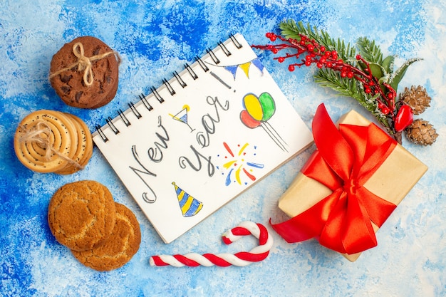 Vista dall'alto capodanno scritto sui biscotti del blocco note legati con una confezione regalo di corda caramelle natalizie sul tavolo blu