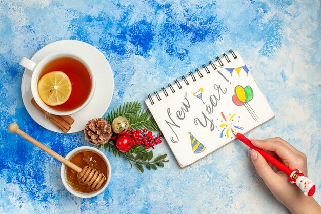 青いテーブルの上のボウルにお茶の蜂蜜の女性の手のカップのメモ帳のペンに書かれた上面図新年