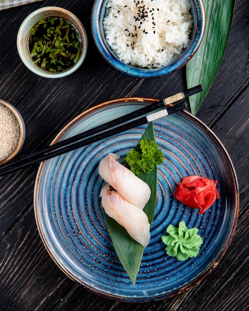Top view of nigiri sushi on bamboo leaf served with ginger and wasabi on a plate