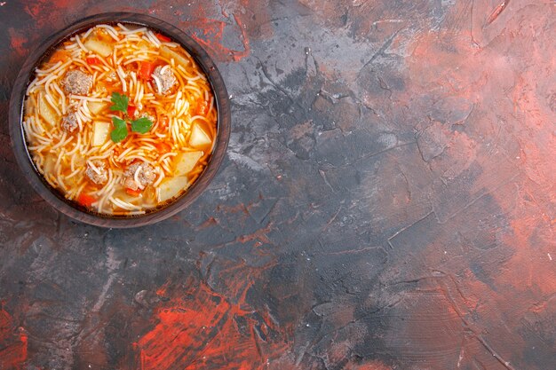 Top view of noodle soup with chicken in a brown bowl on the right side of the dark background