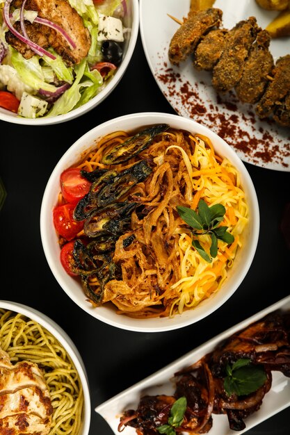 Top view noodles with fried vegetables with tomatoes salad and other dishes on the table
