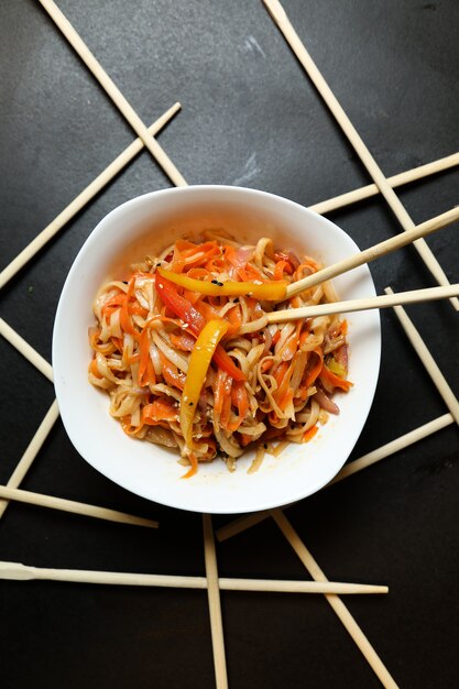 Top view noodles with vegetables in a plate and chopsticks