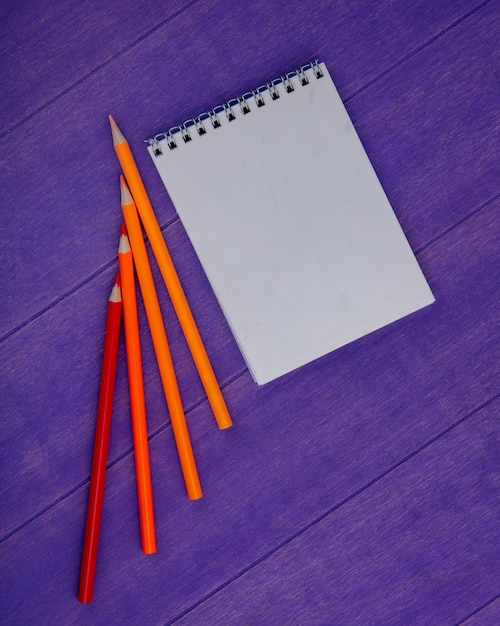 Free photo top view of note pad and colored pencils on purple background with copy space