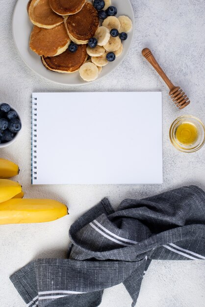 Top view of notebook and breakfast pancakes with banana slices and blueberries