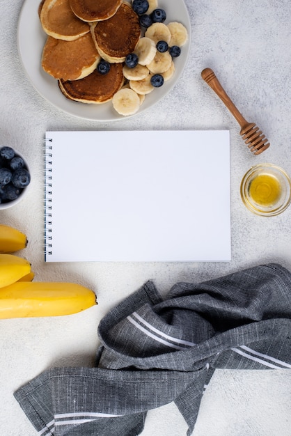 Top view of notebook and breakfast pancakes with banana slices and blueberries