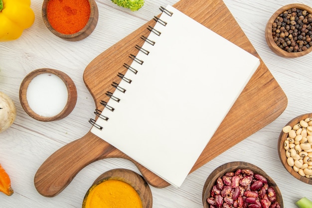 Top view notebook on chopping board different spices in bowls on table