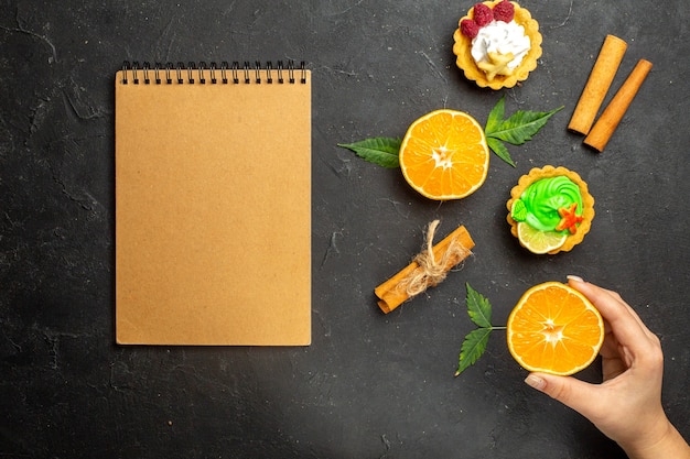 Top view of notebook delicious cookies cinnamon limes and half cut oranges with leaves on dark background