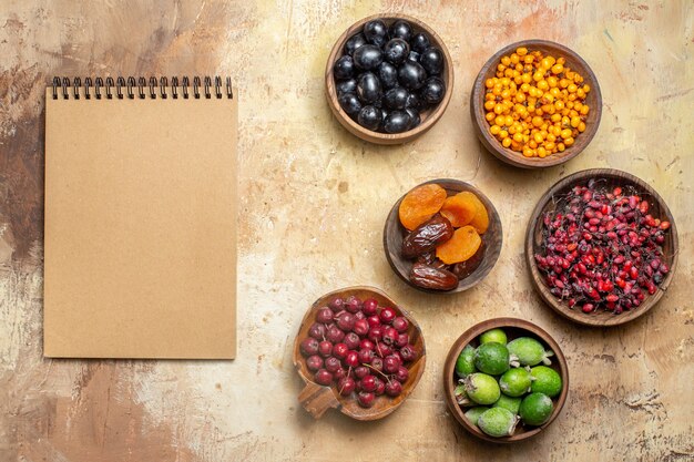 Top view of notebook and fresh various fruits in small brown pots