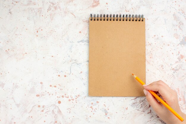 コピースペースと明るい孤立した表面上の女性の手でトップビューノートブックオレンジ色の鉛筆